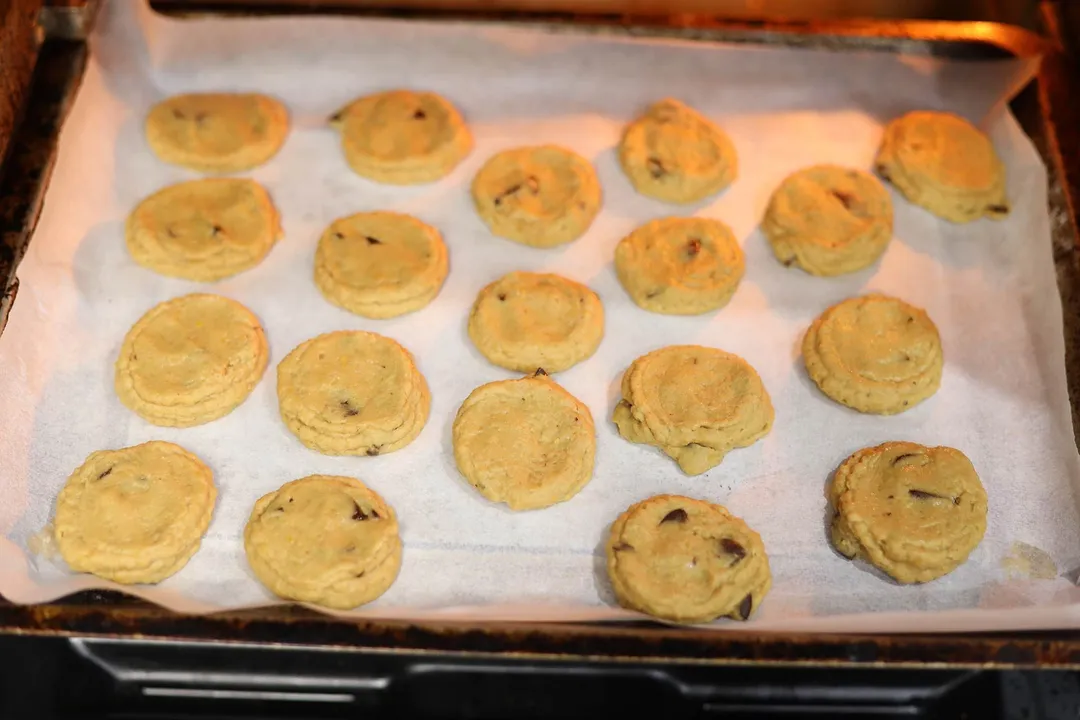 Cookies lined up on a sheetpan lined with parchment paper and baking in the oven.