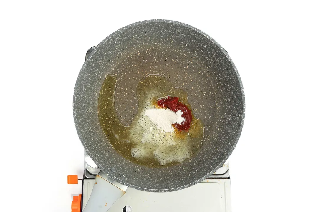 A pan cooking tomato paste and all-purpose flour with olive oil on a portable gas stove.