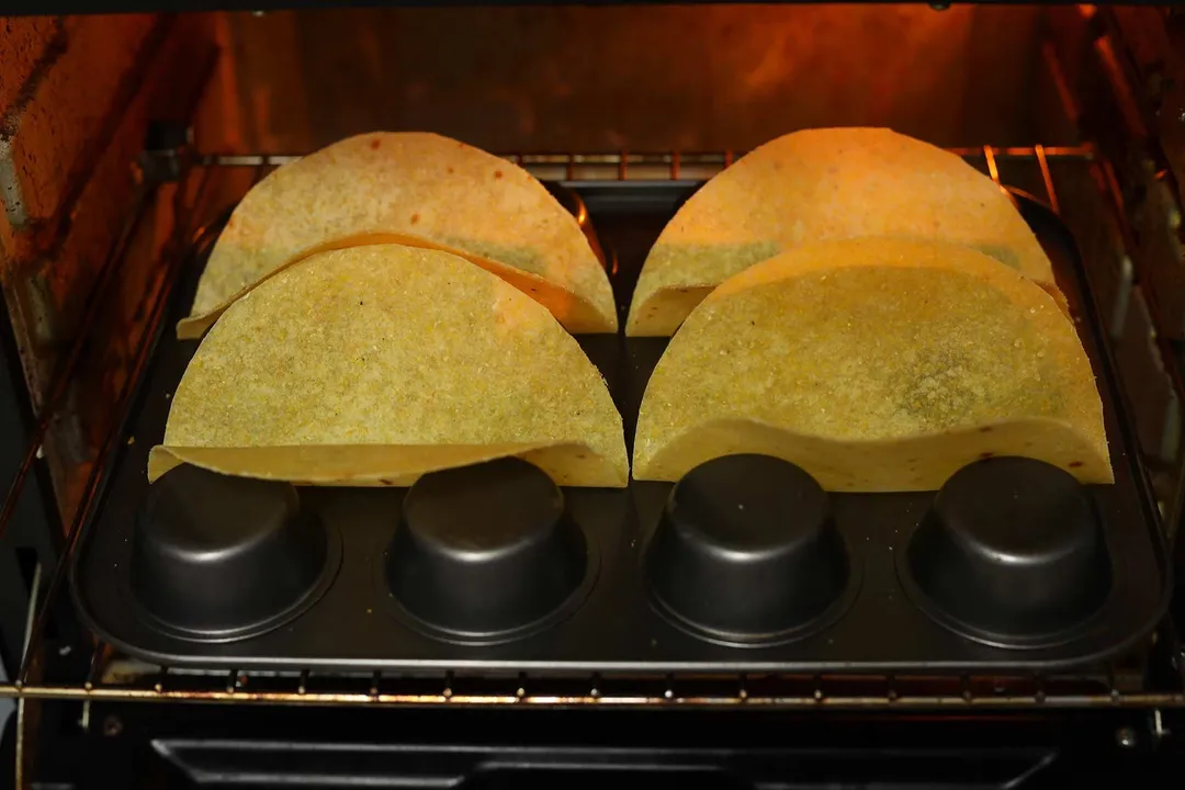 In the oven, four tortillas laid in the crevices of an upside down muffin tray.