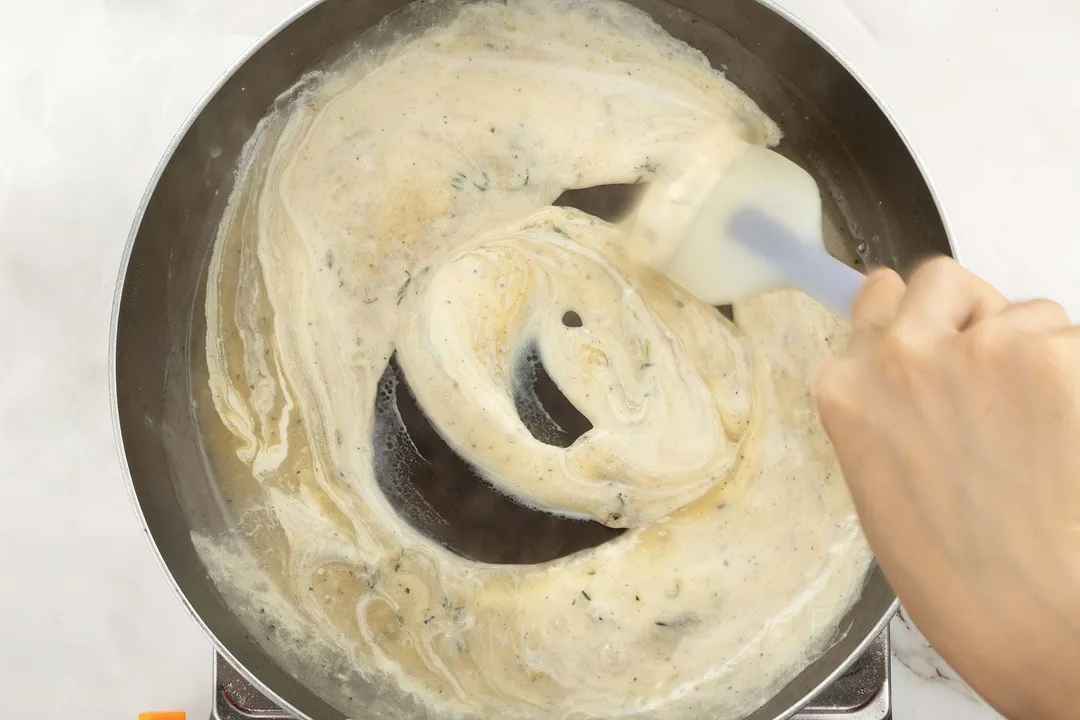 A hand stirring around some heavy cream on a hot pan.