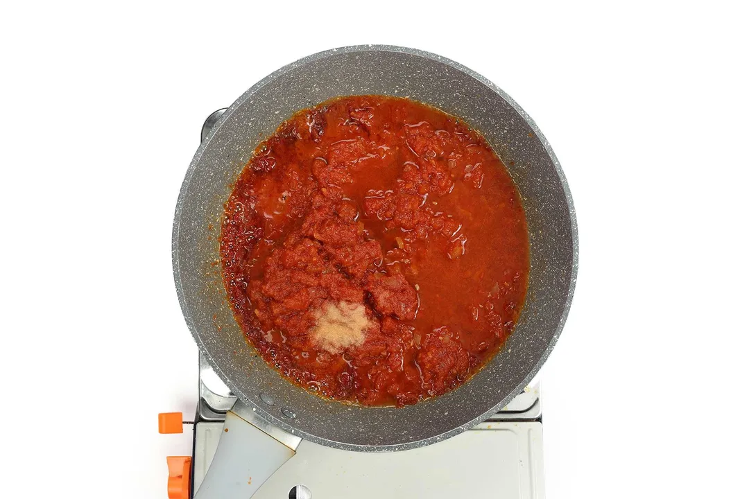 A pan cooking tomato sauce on a portable gas stove.