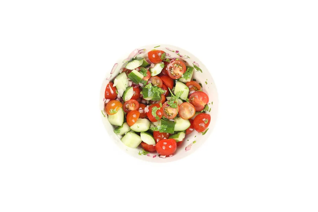 A small bowl filled with cherry tomato halves, cucumber cubes, and coriander leaves.