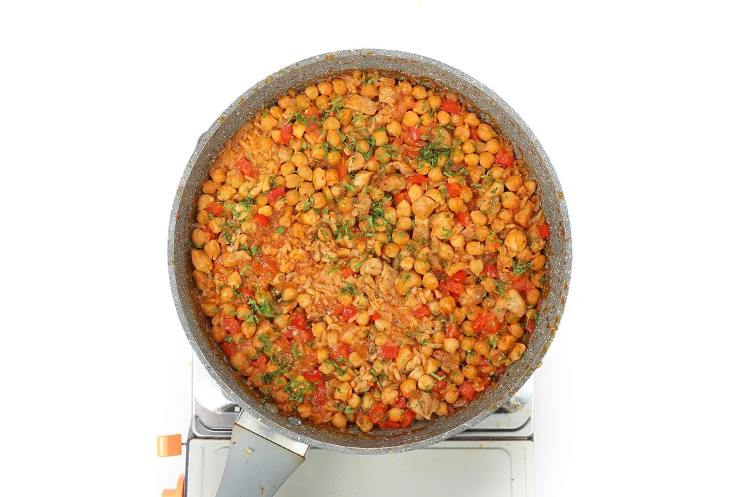 A large pan filled with rice, chickpeas, and diced bell pepper cooking on a portable gas stove.