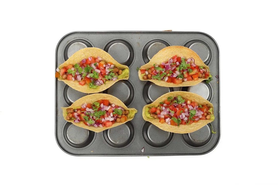 An upside down muffin tray with four chickpea tortillas laid in the crevices.