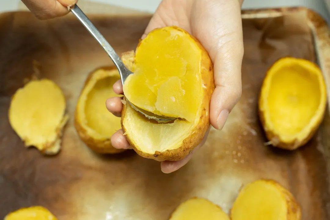 hand holds a spoon to scoop out the inside potato