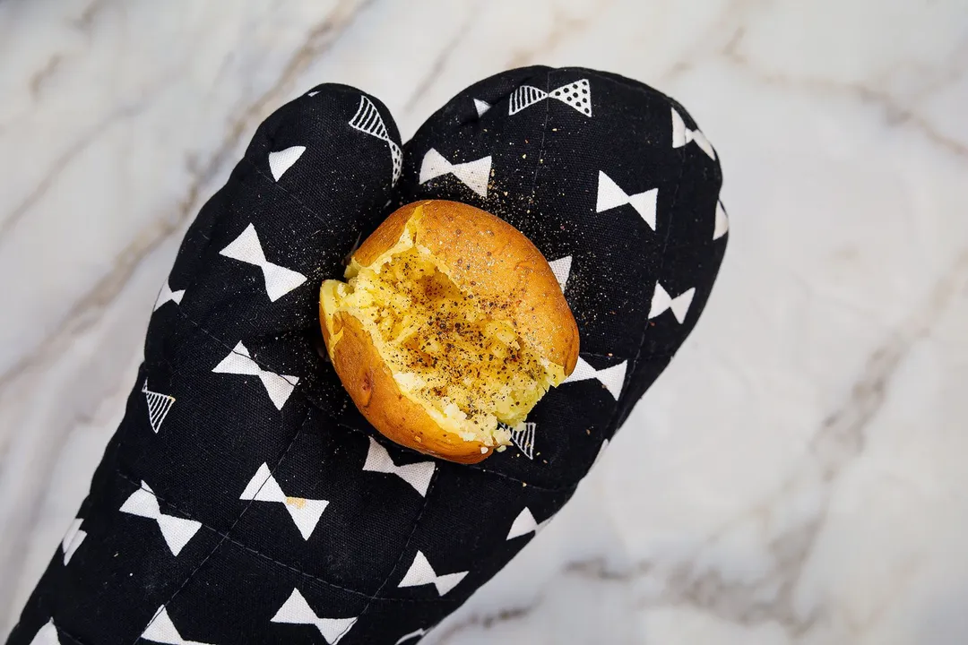 a baked potato seasoned with ground black pepper on a mitten