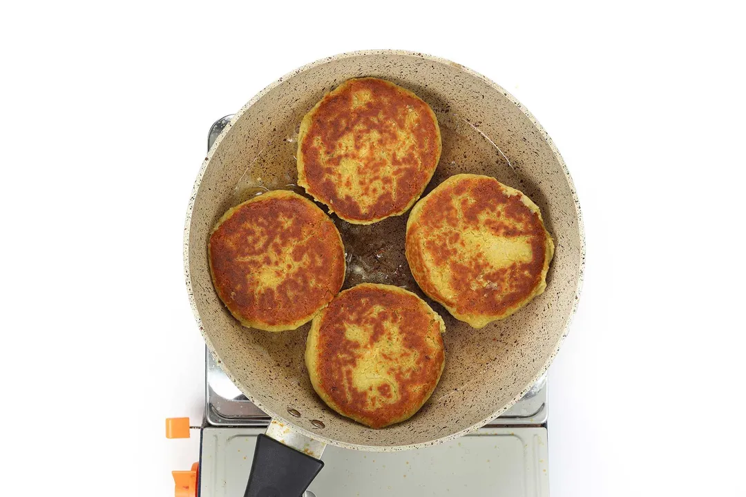 A large pan cooking four hamburger buns on a portable gas stove.