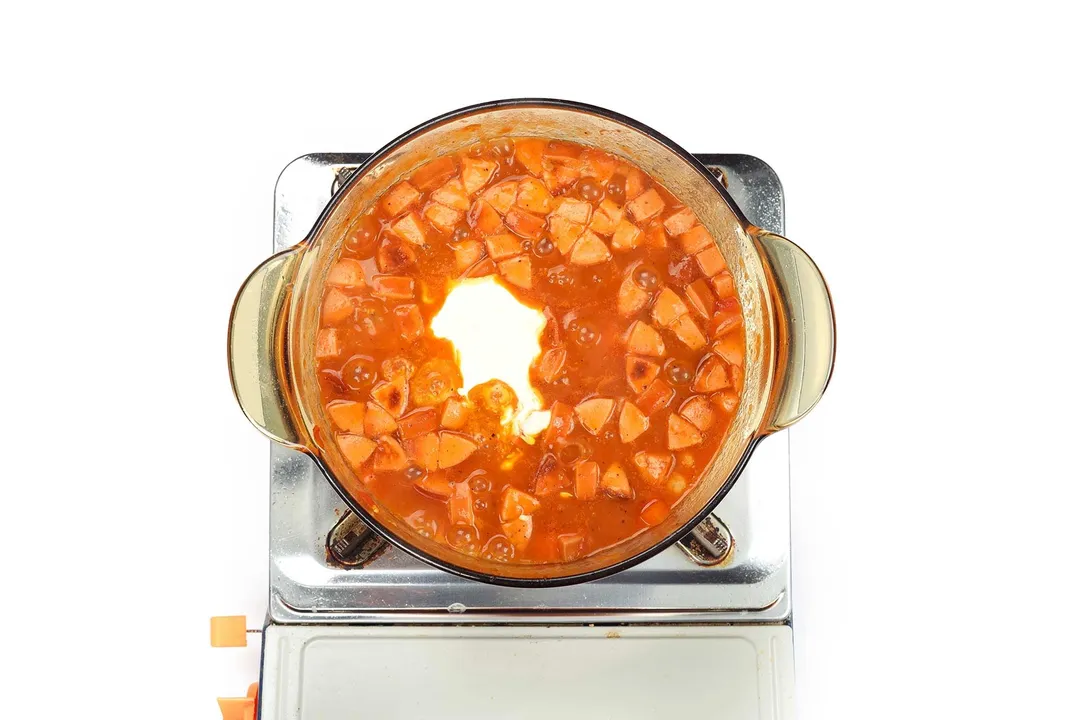 A saucepan cooking chickpea stew with some cream in the middle on a portable gas stove.
