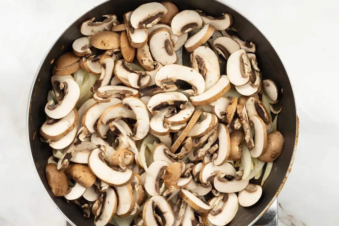 A hot pan cooking sliced mushrooms.