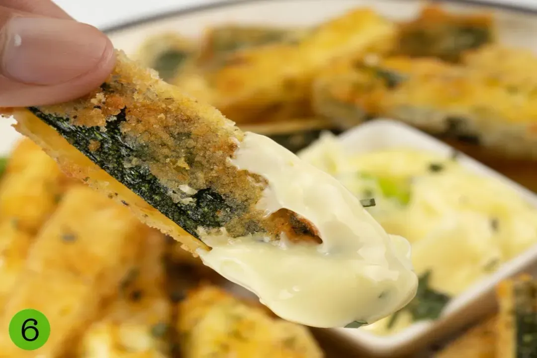 A mayonnaise dipping put inside a plate of zucchini fries, garnished with chopped herbs