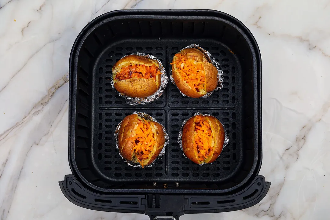 four potatoes with cheese on top in an air fryer basket