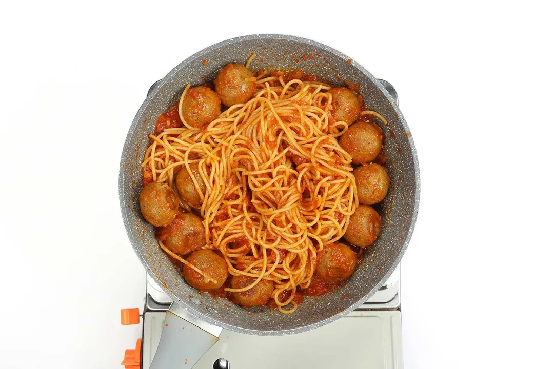 A pan cooking spaghetti and chickpea meatballs on a portable gas stove.