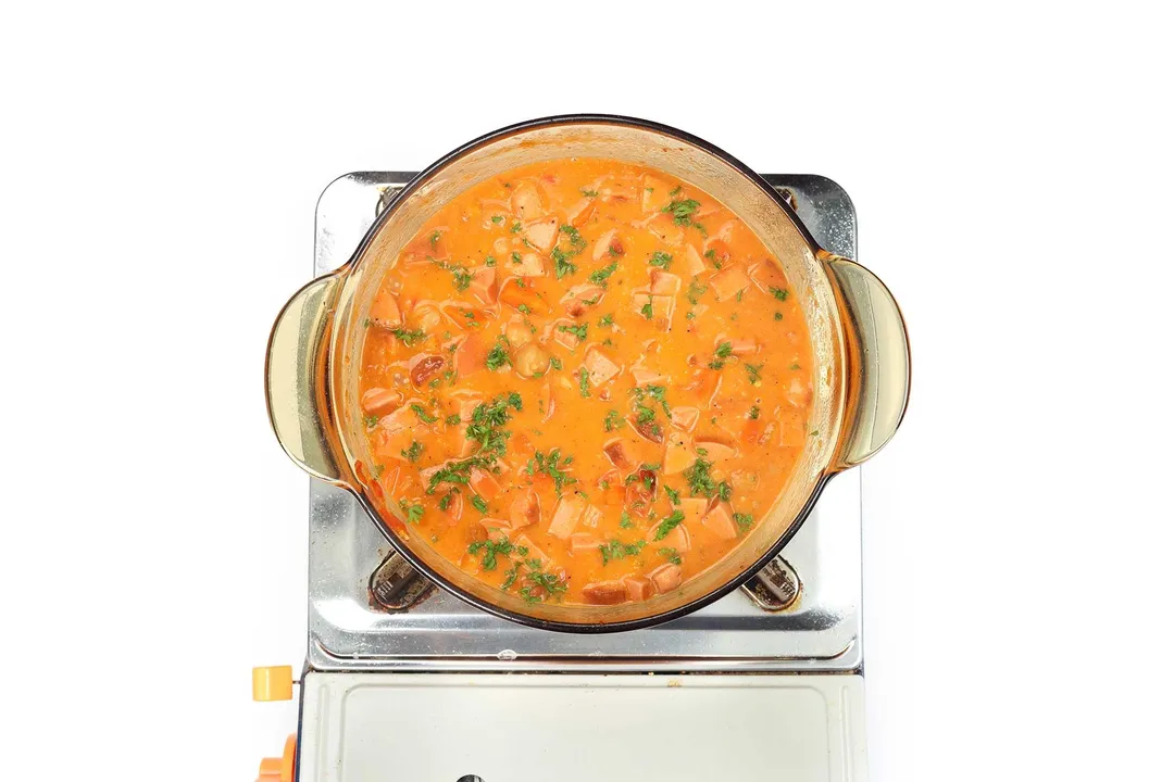 A saucepan cooking chickpea stew garnished with chopped parsley on a portable gas stove.