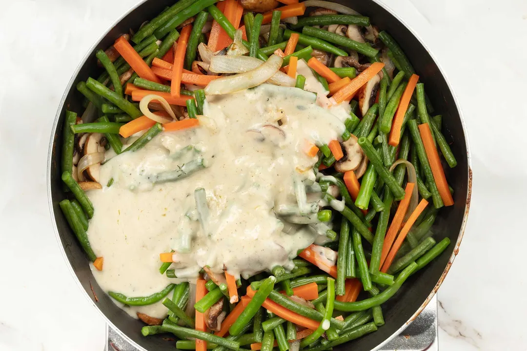 A pan cooking green beans, julienned carrots, and some cream.