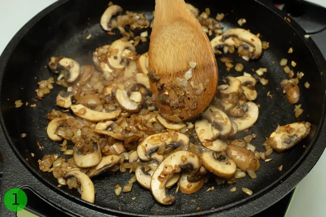 Sliced button mushrooms sautéed in a cast iron skillet with chopped onion