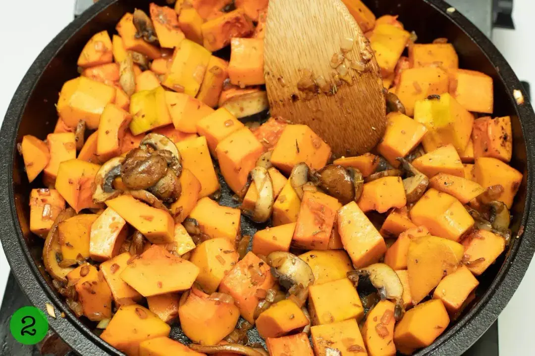 Cubed butternut squash mixed with pieces of mushrooms in a black cast iron skillet