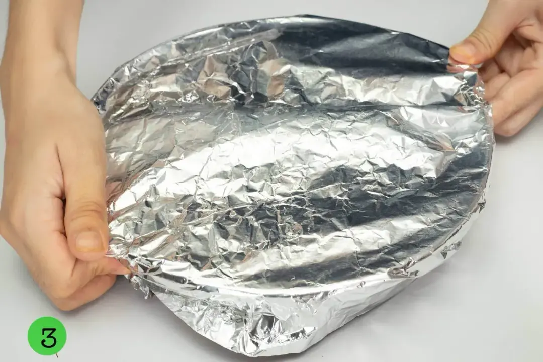 A round baking dish covered in foil, held by two hands