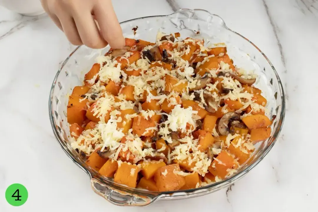 A round baking dish of baked butternut squash with shredded mozzarella cheese scattered on top