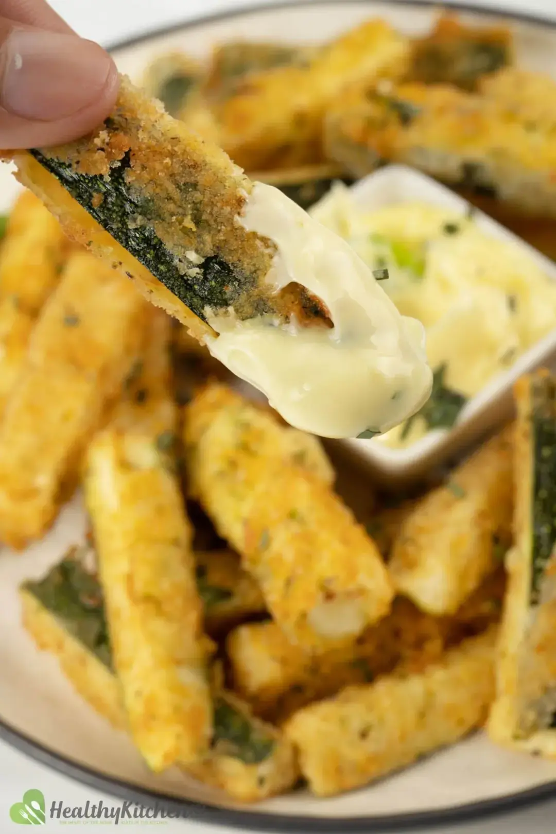 One zucchini fry dipped in mayonnaise, above a background full of zucchini fries
