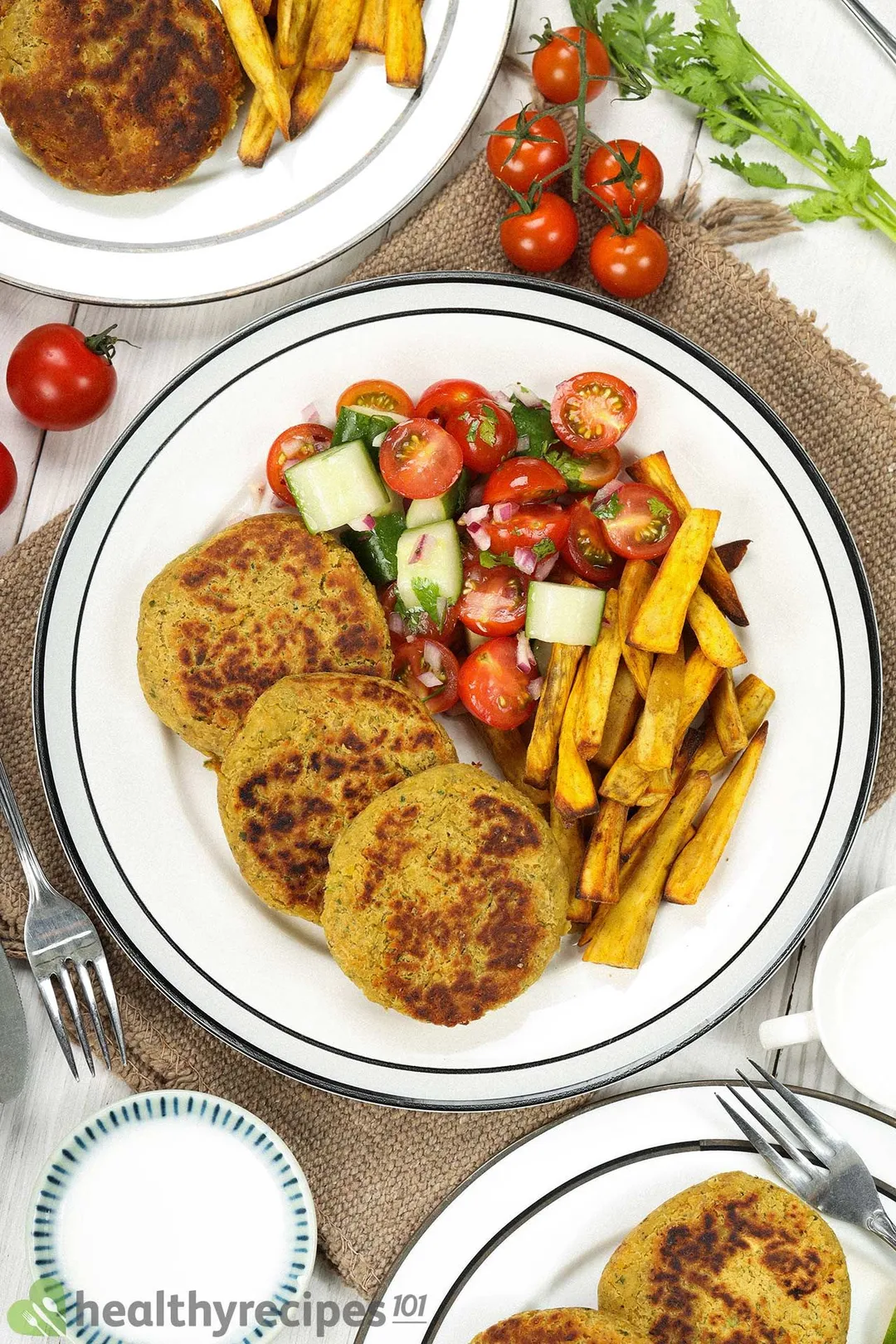 A high-angle shot of plates of chickpea patties, sweet potato sticks, tomato halves, and cucumber cubes.
