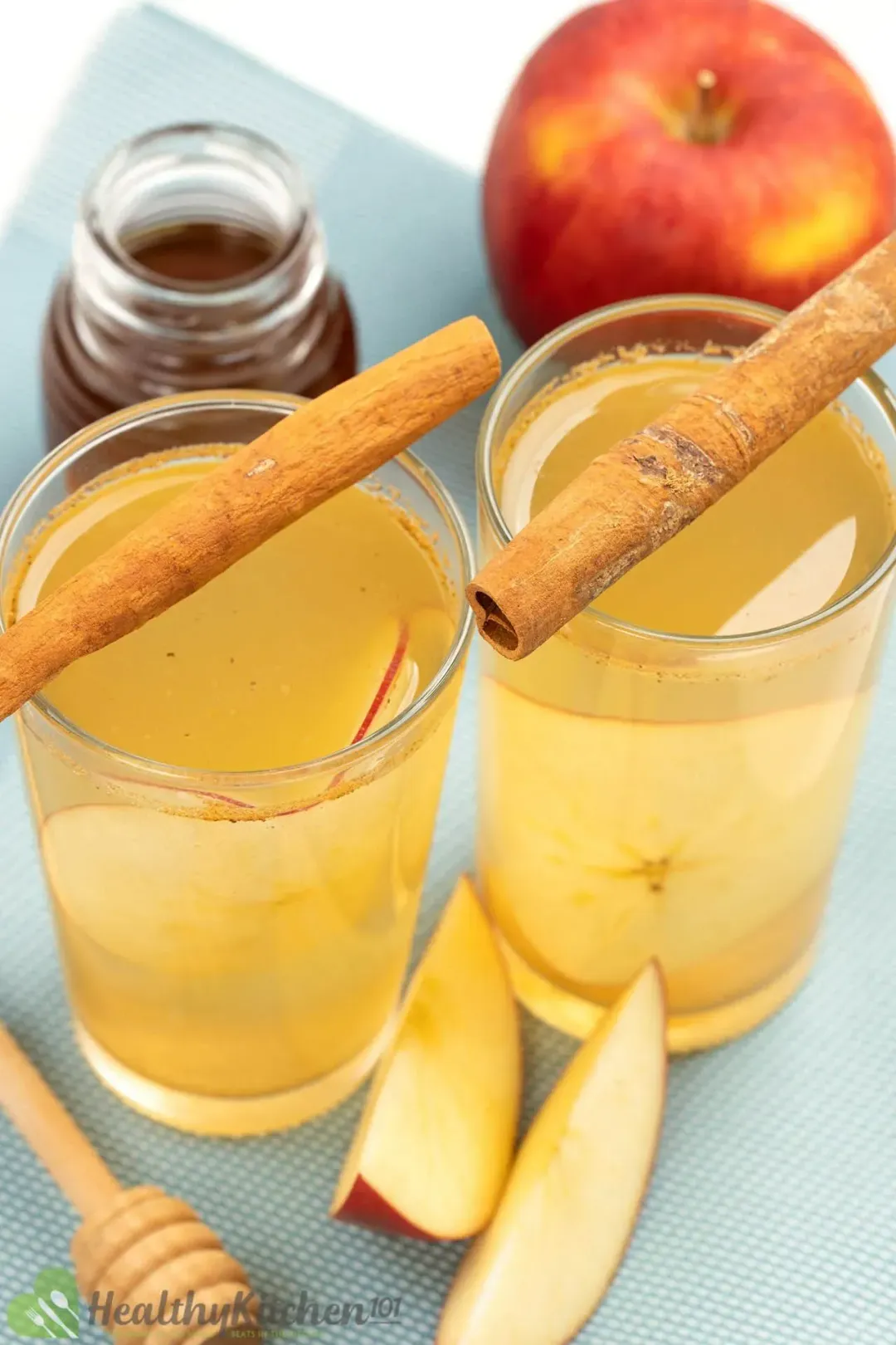 Shot glasses with cinnamon sticks on top, apple wedges on the side, and an apple in the back
