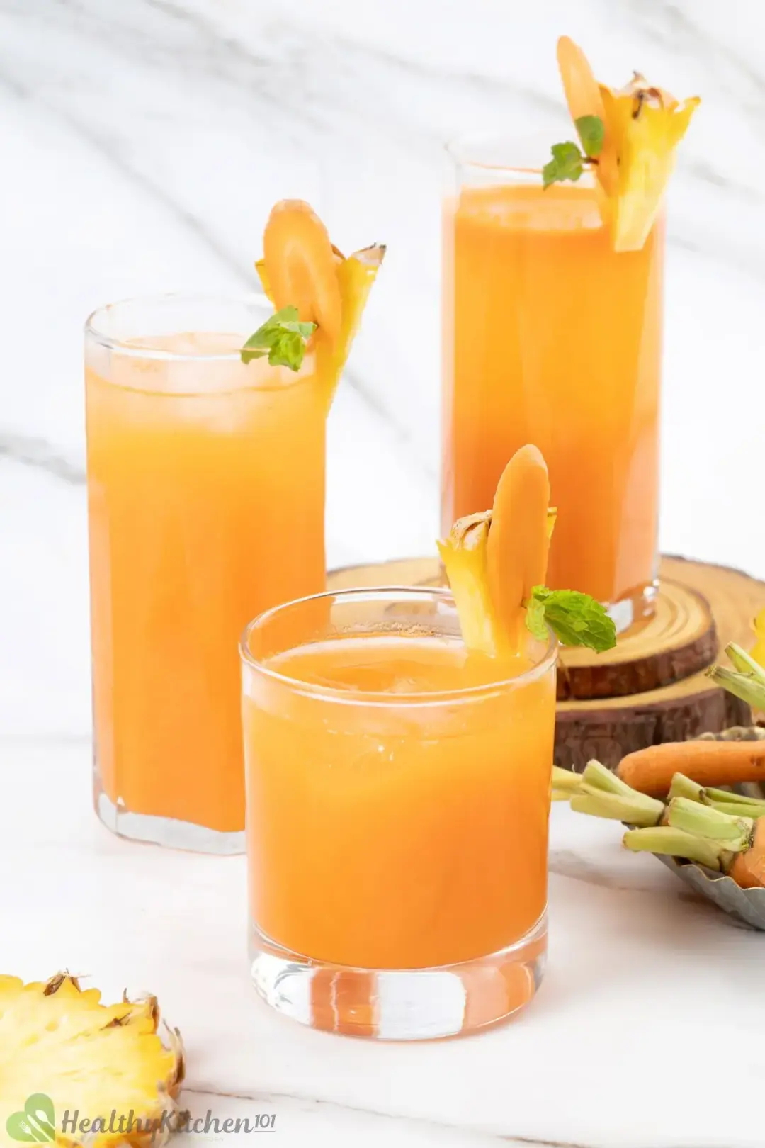 Three glasses of pineapple orange carrot juice of different sizes garnished with carrot slices pineapple wedges and baby carrots