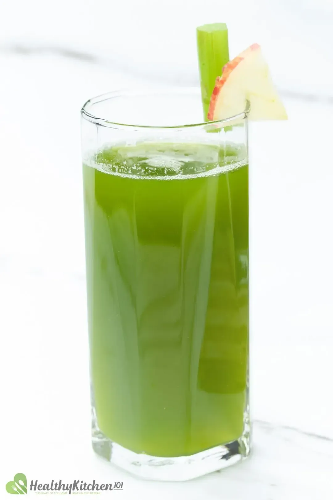 A glass of celery juice, with an apple slice and a celery stalk on the rim