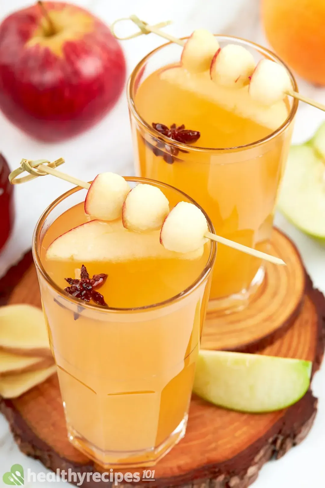 two glasses of apple cider hot toddy decorated with apple sliced, ginger sliced and an apple