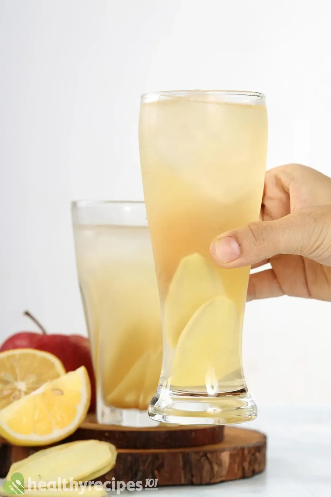 A hand putting a glass of apple cider vinegar drink next to another glass of the same drink