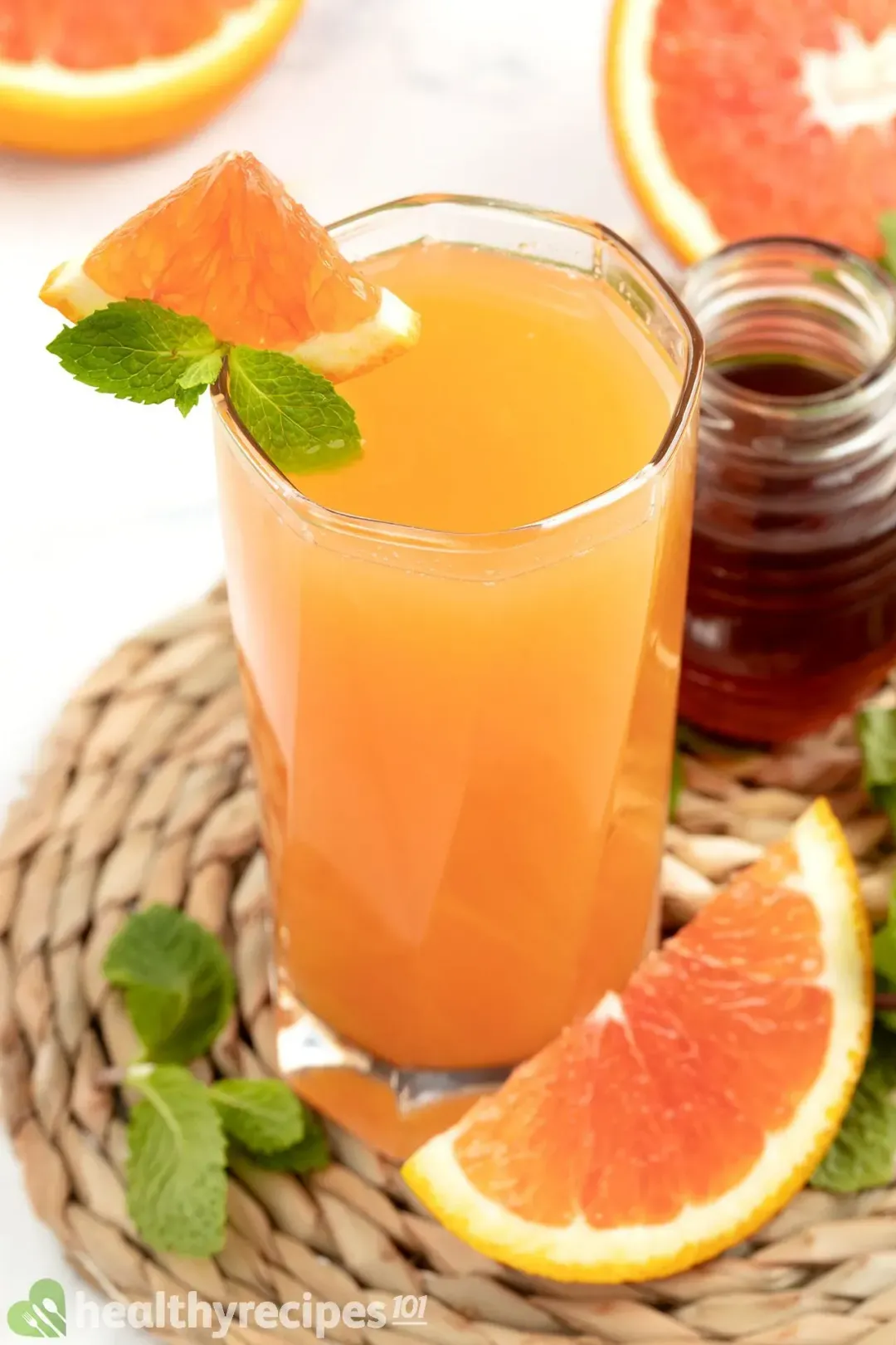 A glass of grapefruit juice garnished with mints, grapefruit wedges, next to a honey jar