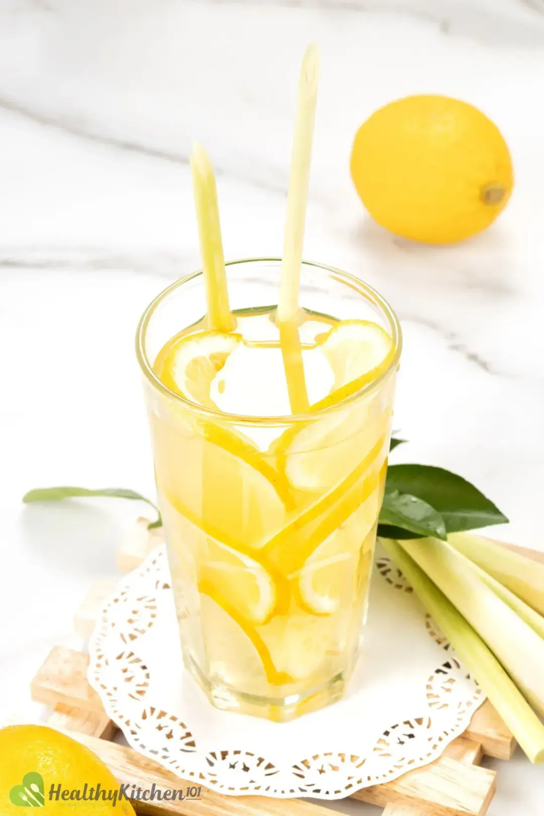 A drink of lemon juice and cider full of lemon wheels put next to lemongrass stalks and lemon leaves