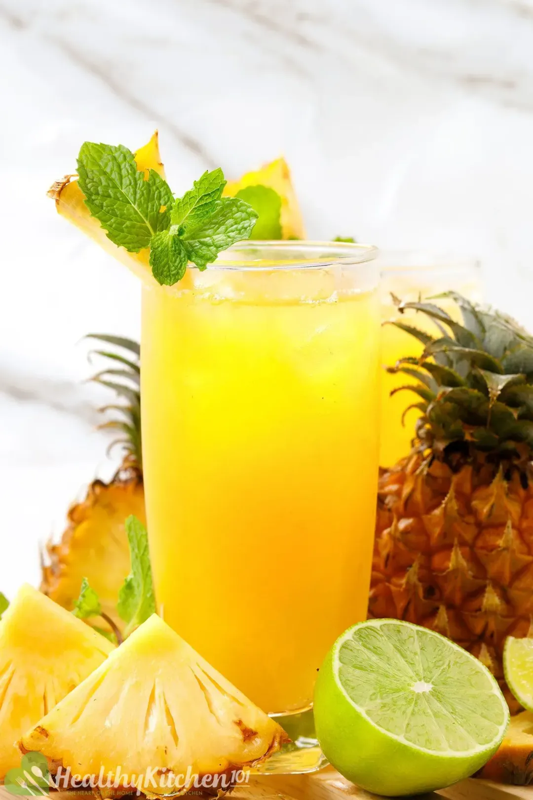 A glass of pineapple juice cocktail garnished with mints, lime halves, and pineapple wedges