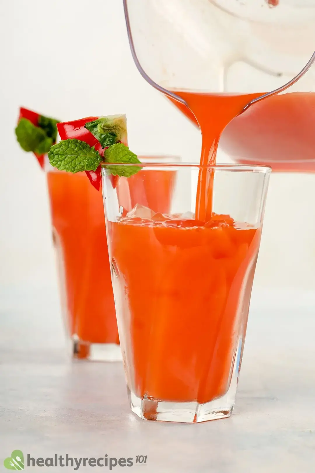 A glass of bell pepper juice garnished with mints, next to another glass being poured pepper juice from a pitcher
