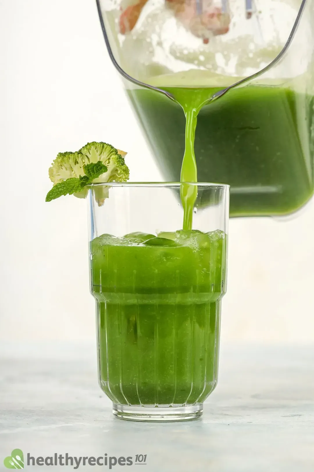 A glass of broccoli juice drink poured from a pitcher above it