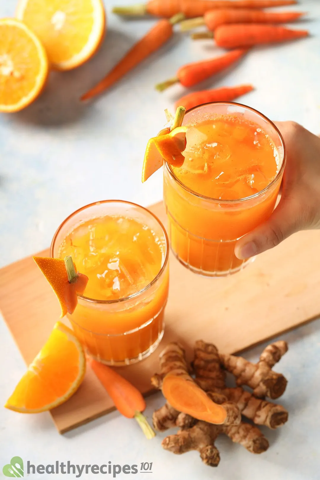 two glasses of carrot turmeric juice, a hand holds one.