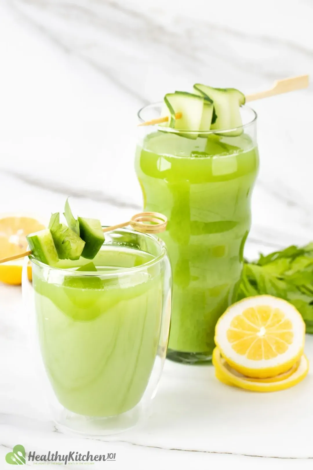 Two glasses of cucumber celery drink, each with a skewered strand of cucumber slice on top and next to some lemon wheels