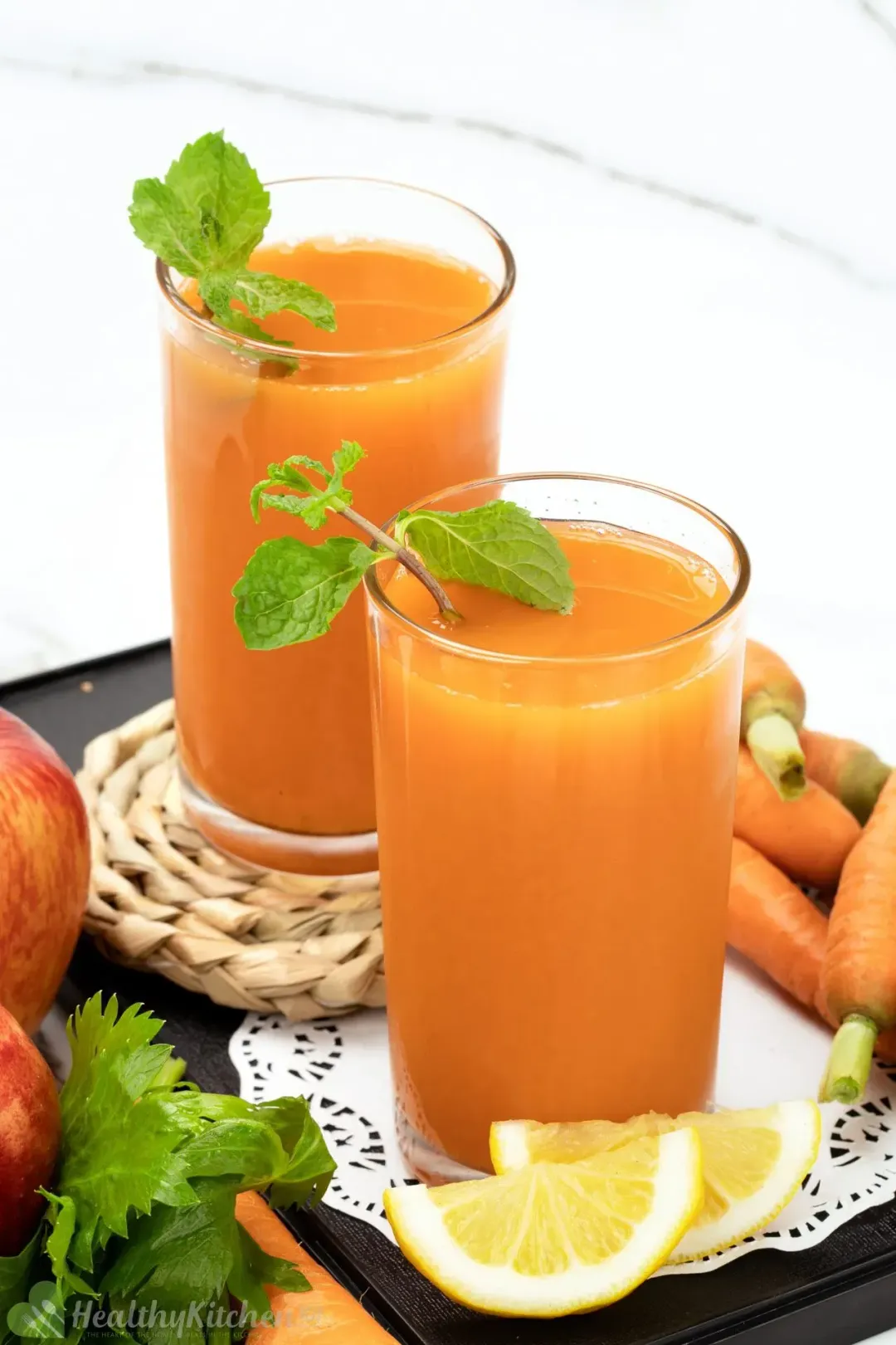 Two glasses of carrots and celery juice garnished with lemon wedges and sprigs of mint