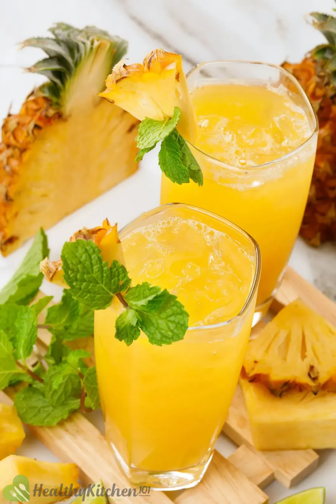 Two glasses of pineapple and apple cider vinegar drinks garnished with mint leaves and pineapple wedges