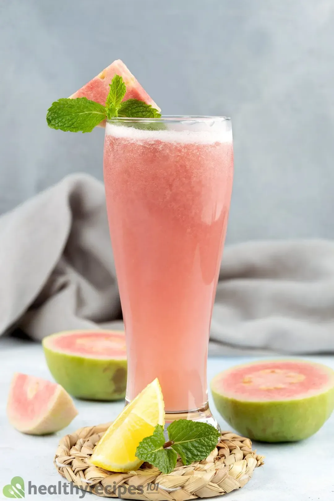 A tall and slim glass of guava juice surrounded by guava slices and a lemon wedge