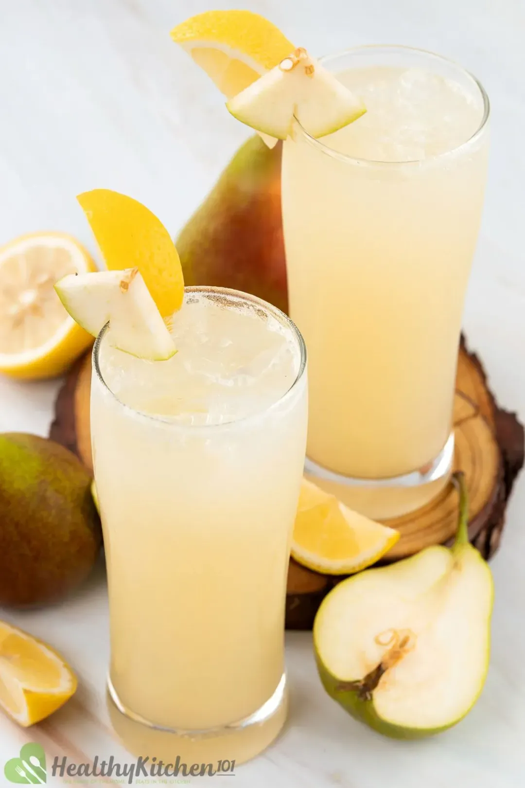 Two glasses of pear juice with ice, garnished with pear halves and lemon wedges