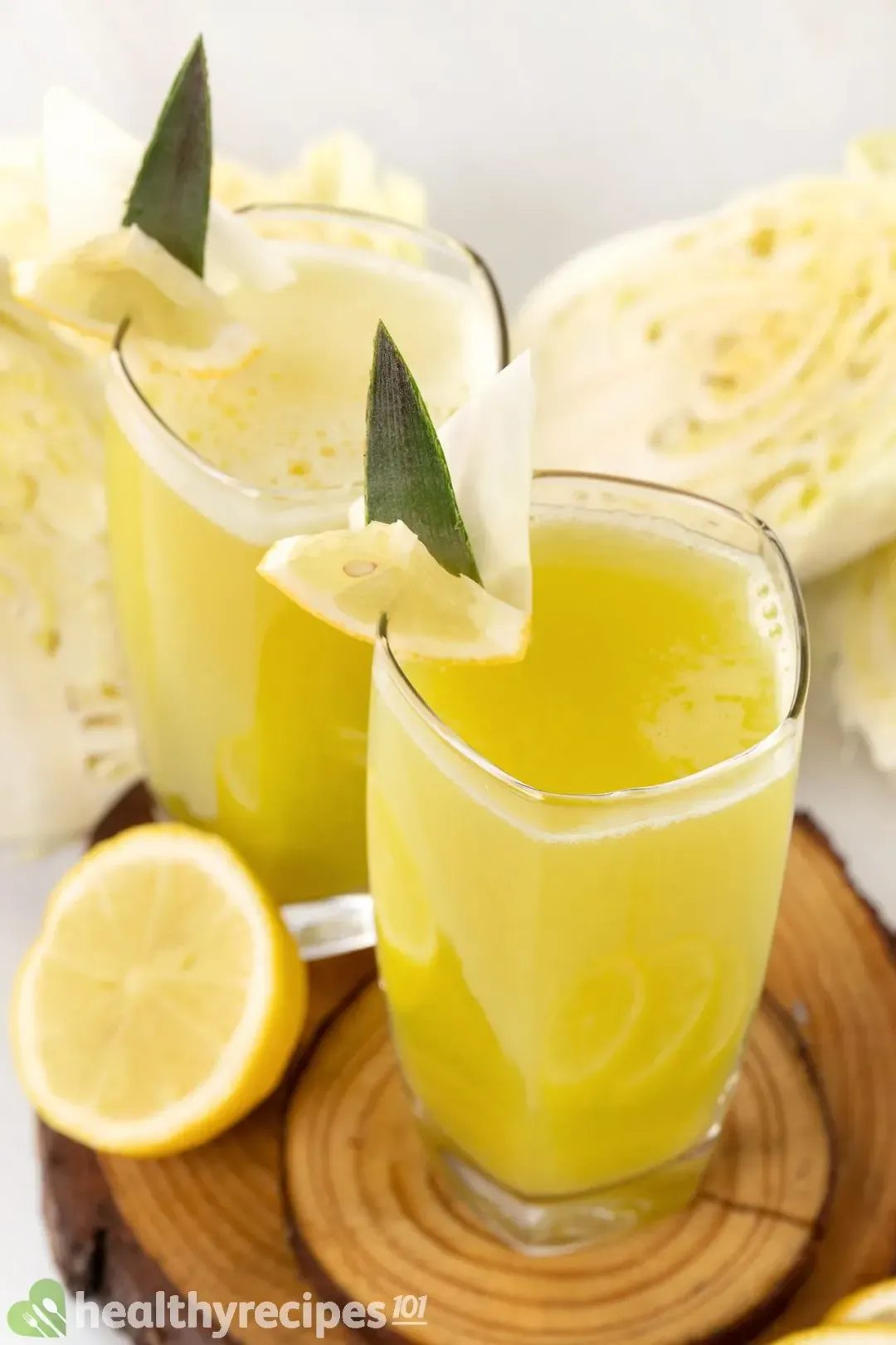 Two glasses of yellow-green cabbage drink garnished with lemon wedges, and put next to half a lemon