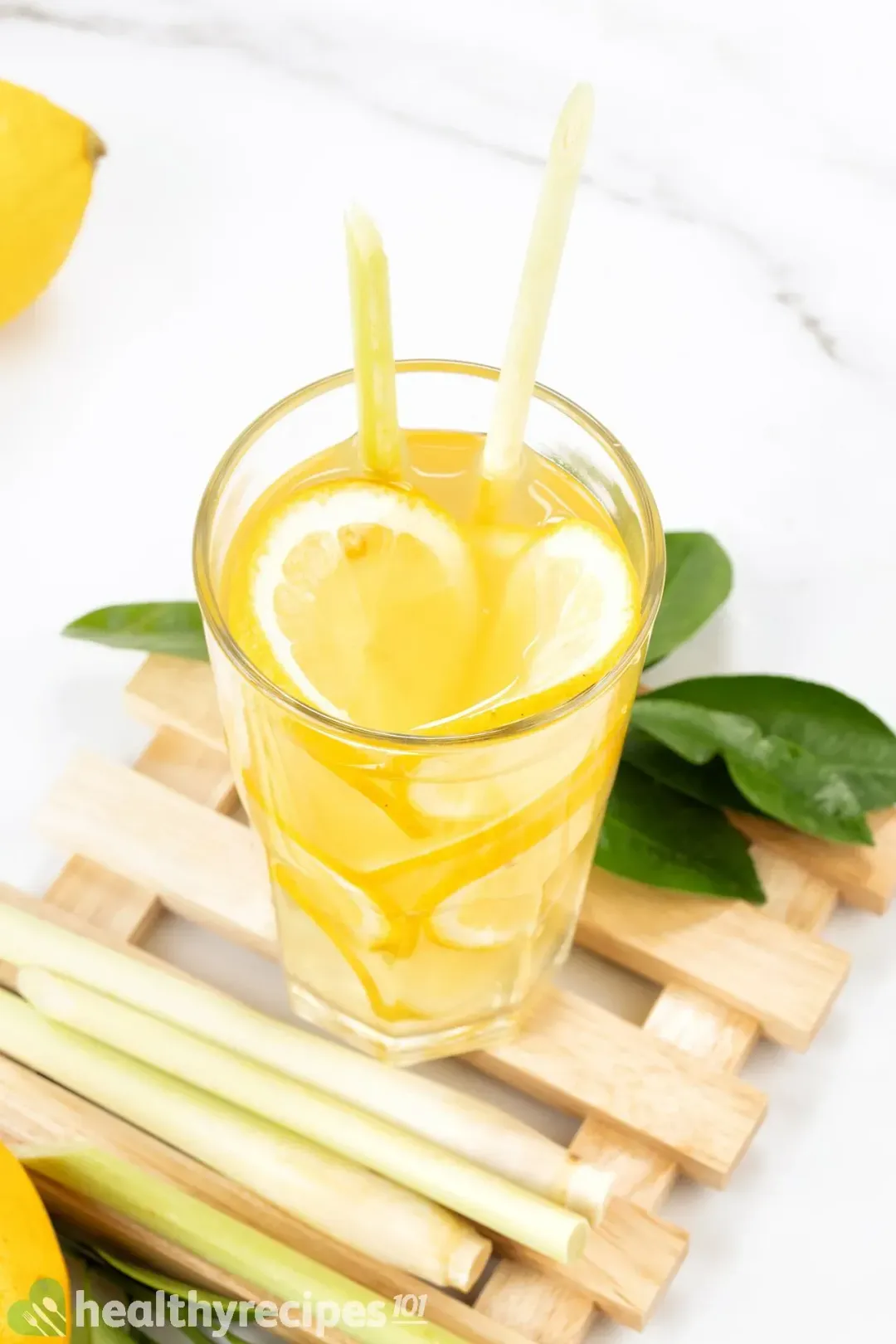 A high glass of lemon vinegar drink packed with lemon wheels, next to lemon leaves and on a wooden coaster