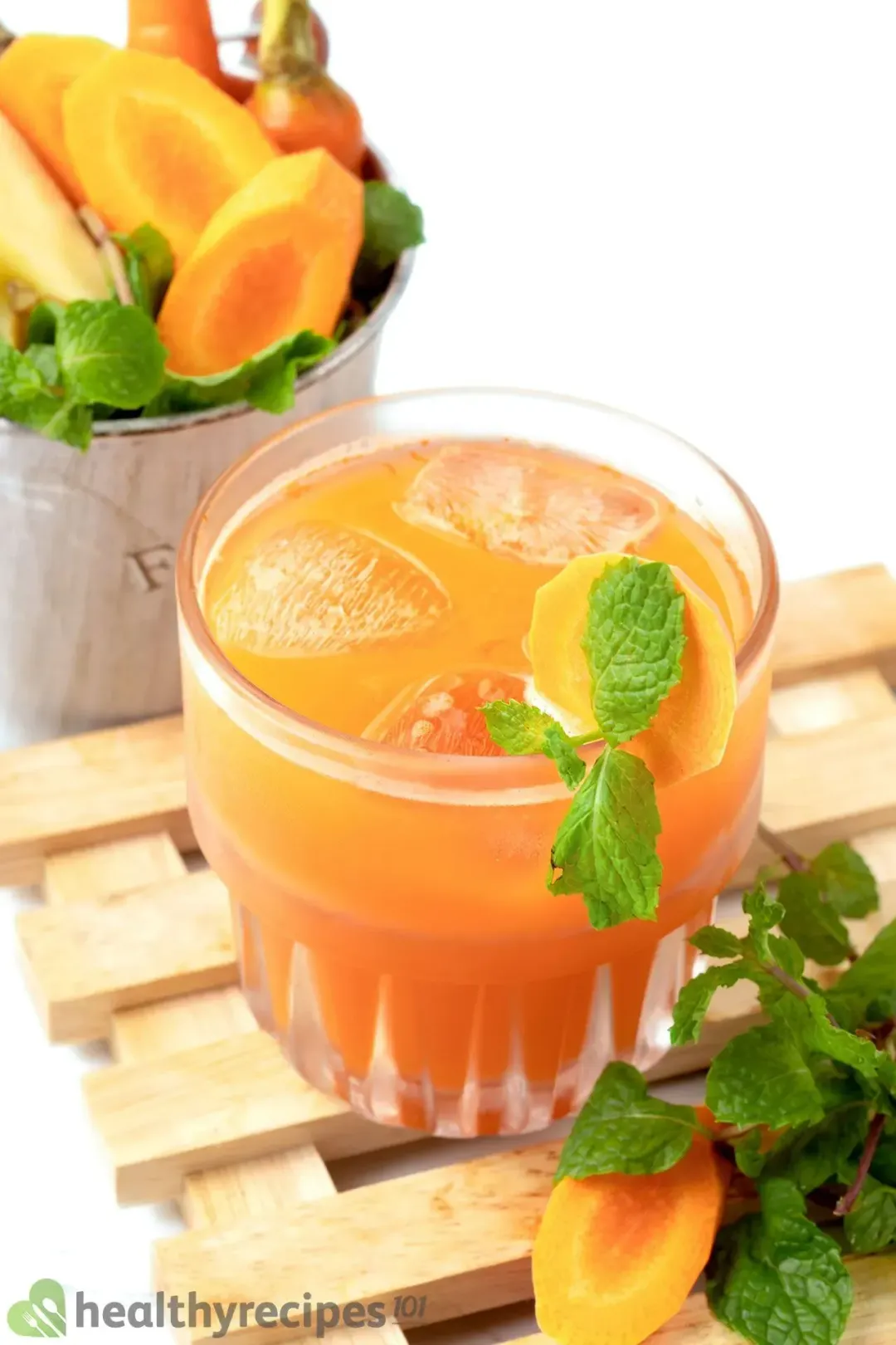 A short class with ice and an orange drink next to mint leaves on a wooden coaster