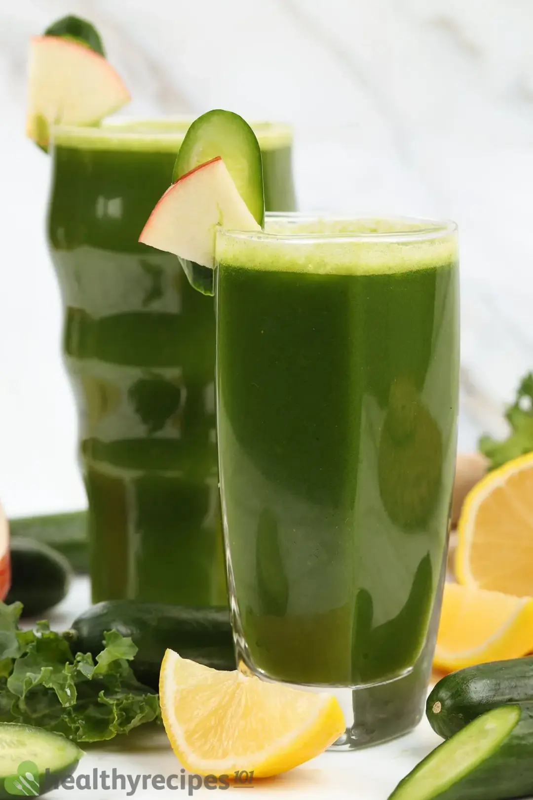 Two glasses of green juice, with fruits and greens around as garnish