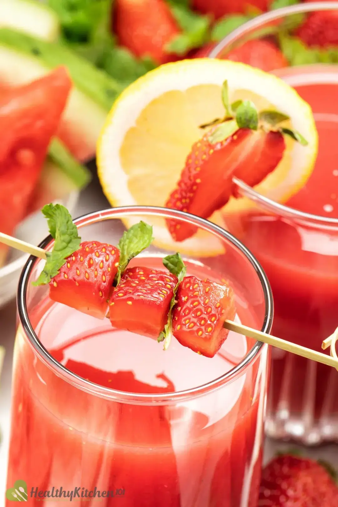 A close-up shot of two glasses of juice decorated with strawberries and a slice of lemon