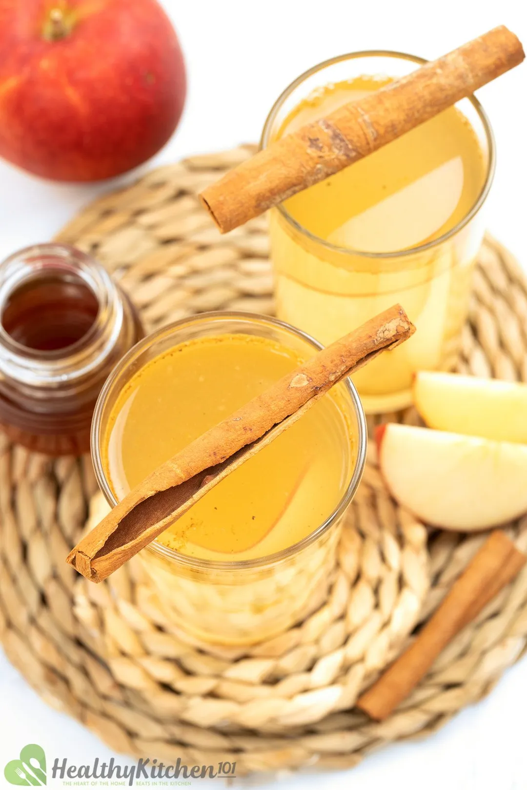2 glasses of Apple Cider Vinegar and Honey garnish with apple, honey jar and cinnamon sticks