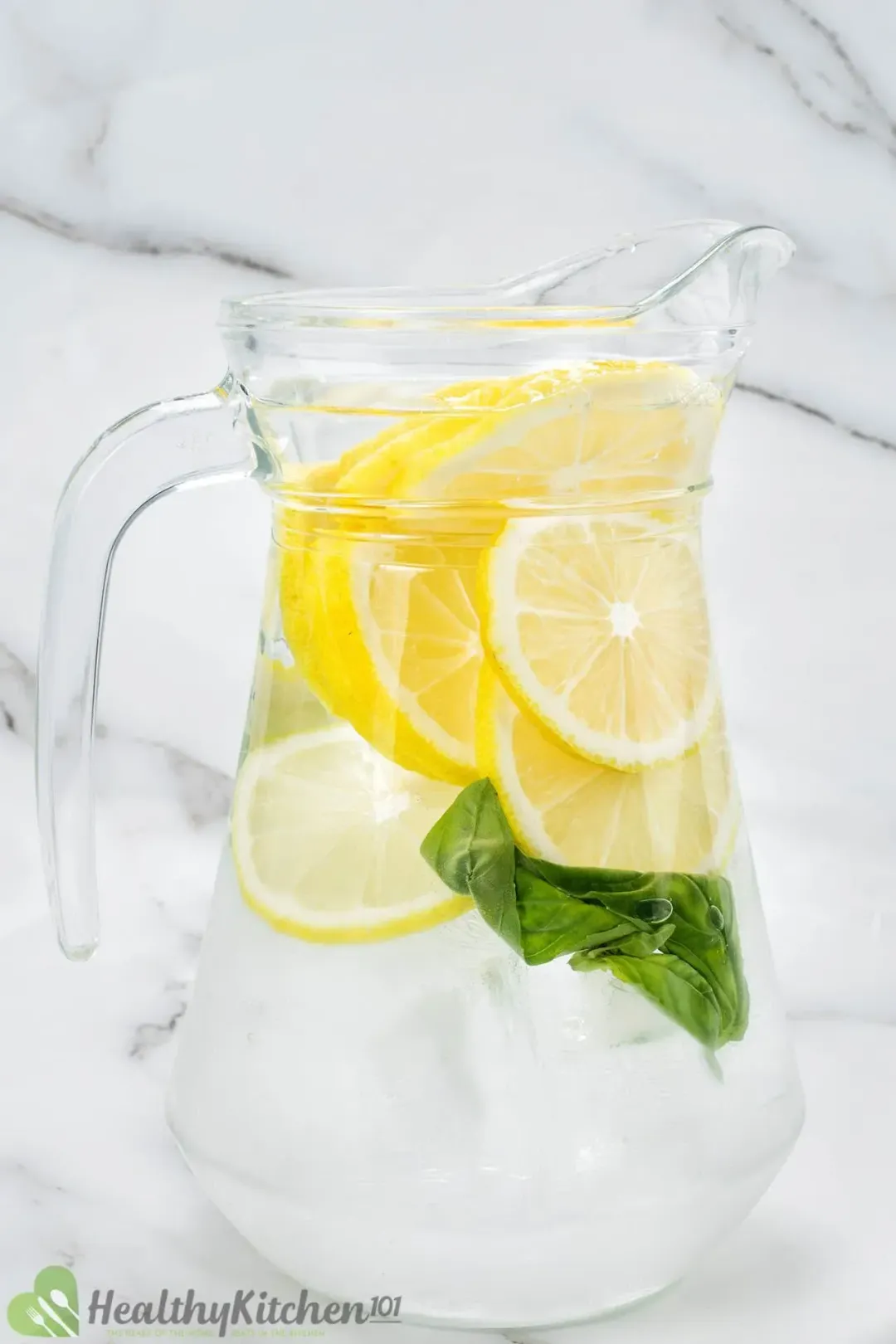 A pitcher of clear water submerging lemon wheels and some basil leaves