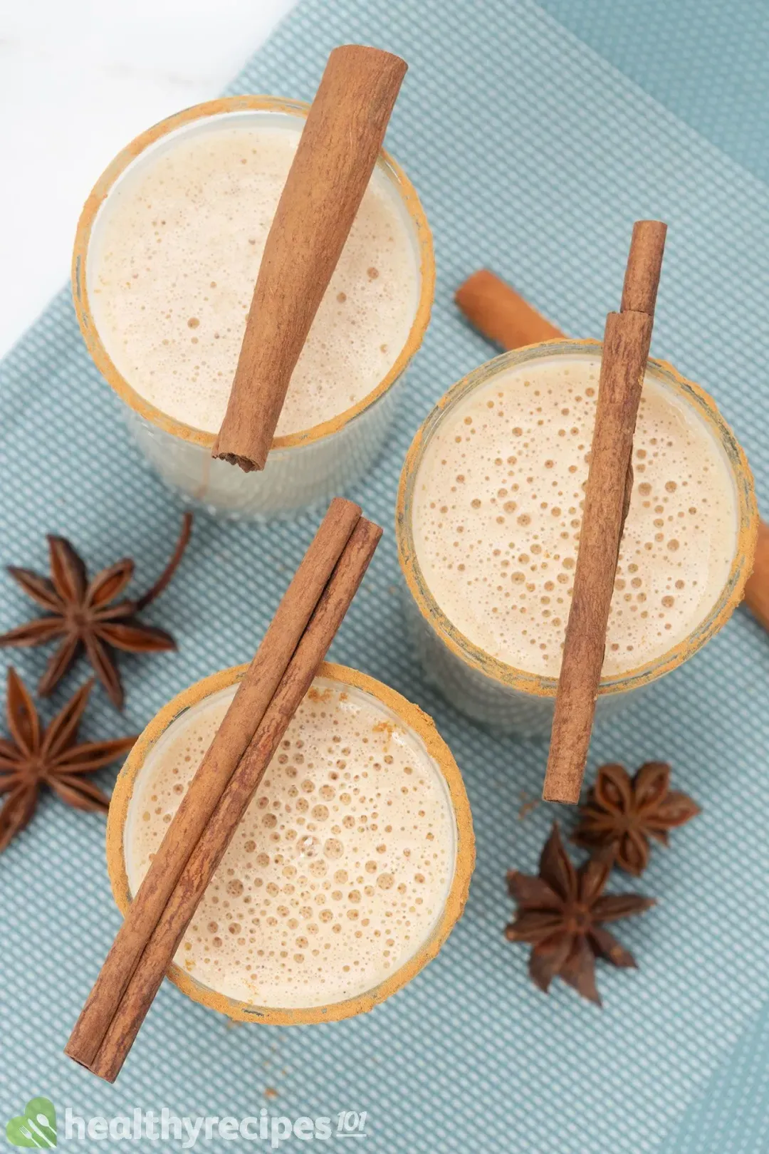 Three classes of foamy eggnog in different sizes topped with cinnamon sticks and surrounded by star anise