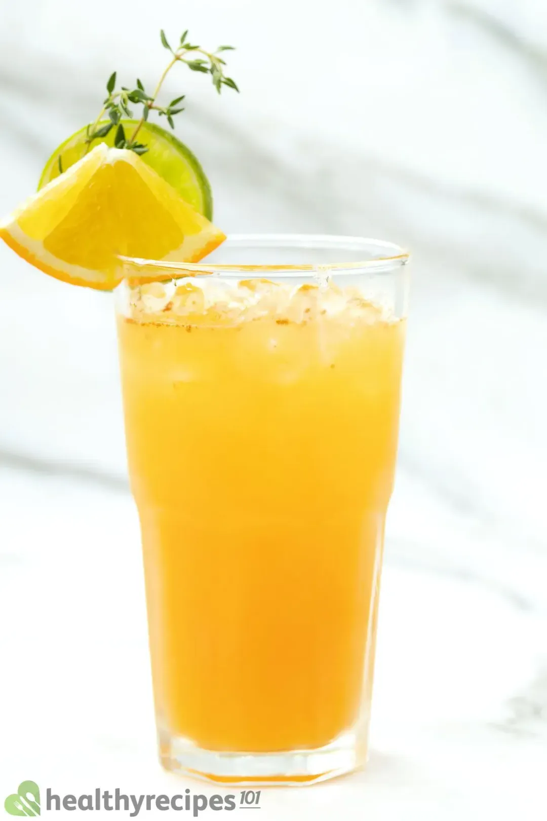 A tall glass of iced orange juice cocktail with lemon wedge and lime wheel on the rim