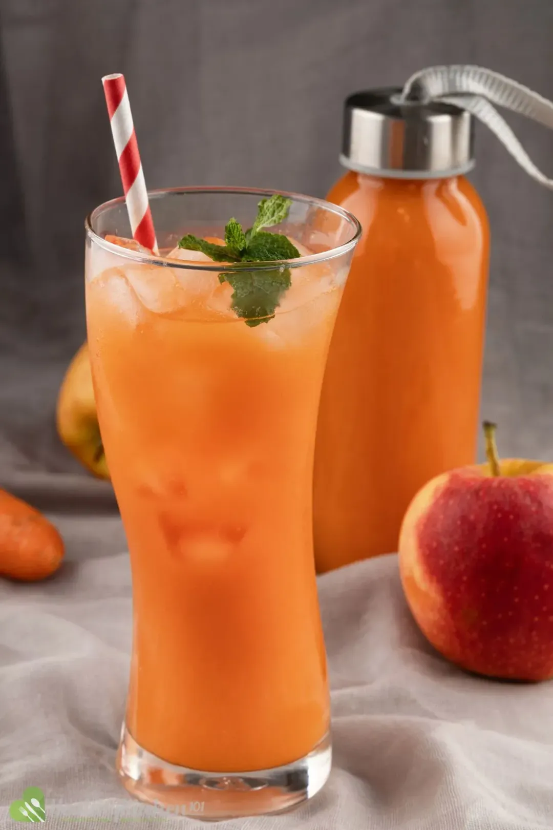An iced glass of carrot juice next to a bottle of carrot juice and a red apple